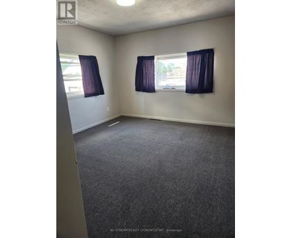 A room with grey carpet and two windows with purple curtains.