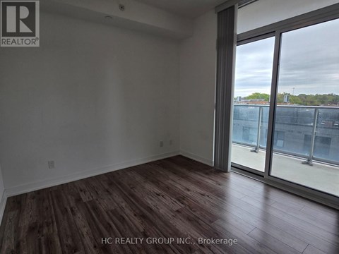A room with wooden flooring and a large window overlooking a fenced area.
