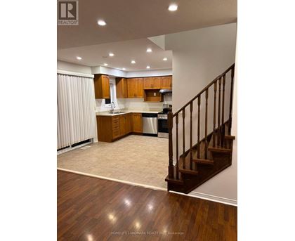 A well-lit kitchen with wooden floors and a staircase.
