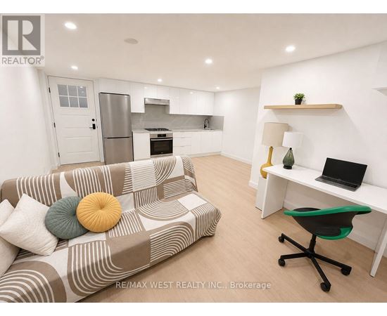 A living room with a couch, a desk, and a kitchen area in the background.