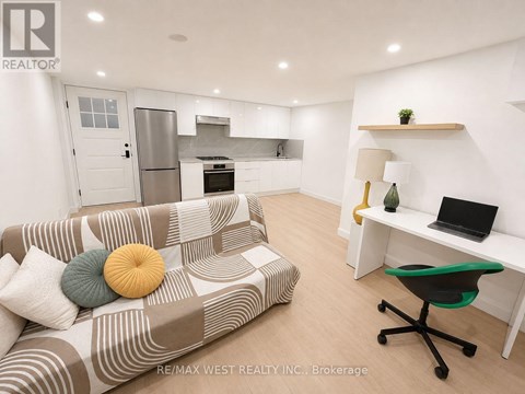 A living room with a couch, a desk, and a kitchen area in the background.