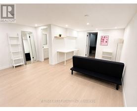 A black sofa sits in a white room with a ladder and a mirror.