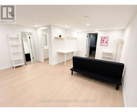 A black sofa sits in a white room with a ladder and a mirror.