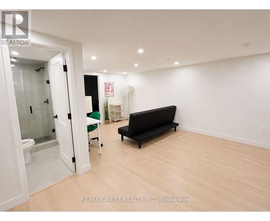 A room with a black couch and a glass door leading to a bathroom.