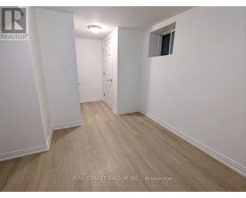 A room with white walls and wooden flooring, with a door on the left and a small window on the right.