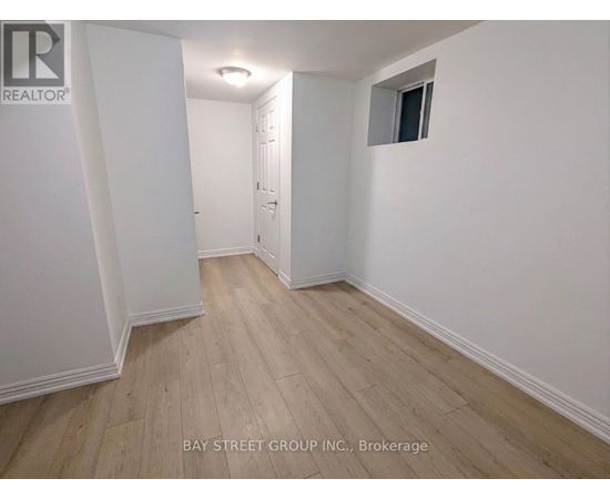 A room with white walls and wooden flooring, with a door on the left and a small window on the right.