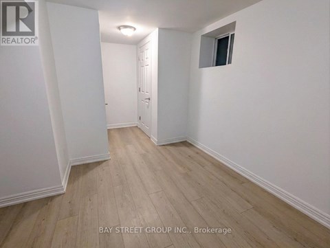A room with white walls and wooden flooring, with a door on the left and a small window on the right.
