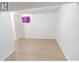 A brokerage listing image of a white room with wood flooring and a pink object hanging on the wall.