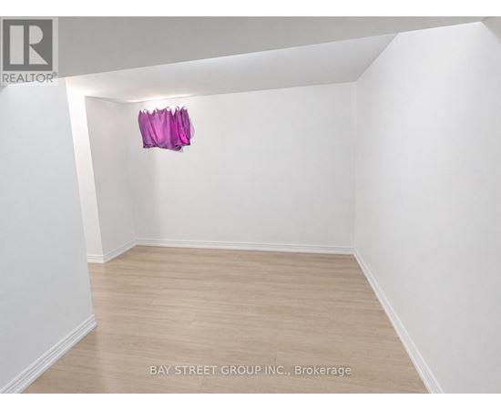 A brokerage listing image of a white room with wood flooring and a pink object hanging on the wall.