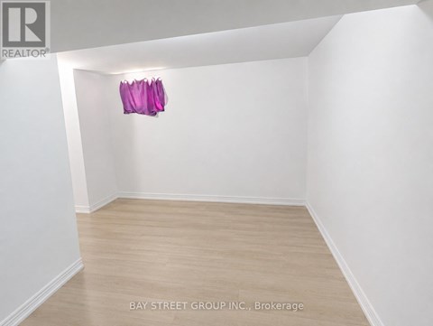 A brokerage listing image of a white room with wood flooring and a pink object hanging on the wall.