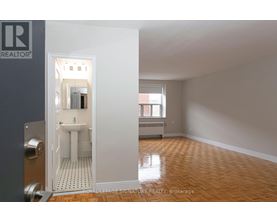 A brokerage sign is on the wall of a room with a toilet and sink visible through an open door.