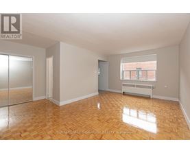 A room with wooden flooring and a window showing a brick building outside.
