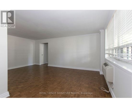 A room with wooden flooring and white walls, with a window on the right side.