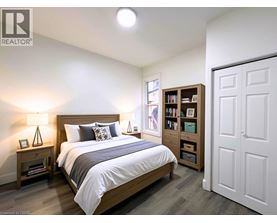 A bedroom with a large bed, a nightstand with a lamp, and a bookshelf.