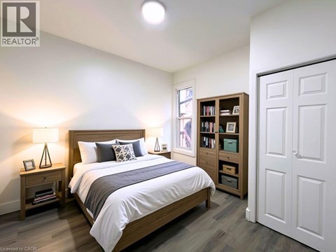 A bedroom with a large bed, a nightstand with a lamp, and a bookshelf.