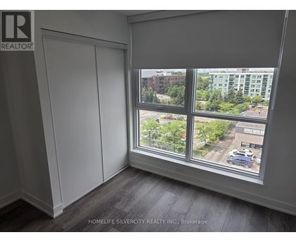 A room with a large window showing a view of a parking lot and buildings outside.