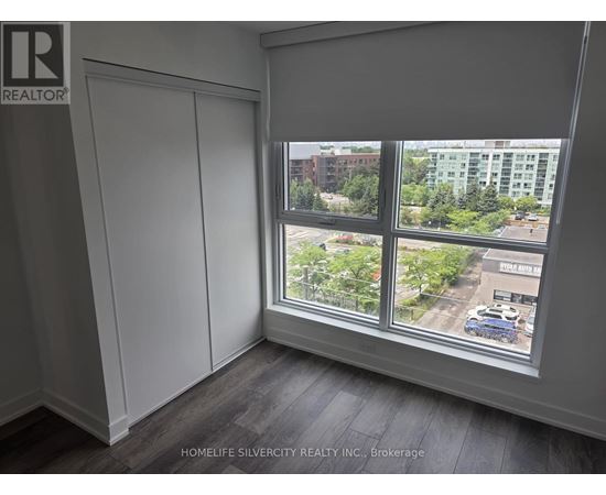 A room with a large window showing a view of a parking lot and buildings outside.