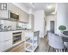A modern kitchen with a white color scheme and a dining area with a grey chair.