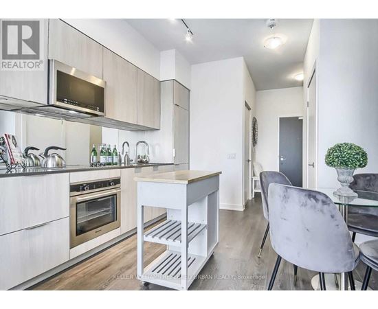 A modern kitchen with a white color scheme and a dining area with a grey chair.
