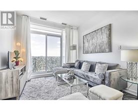 A living room with a grey couch, a glass table, and a large window with a view of the balcony.
