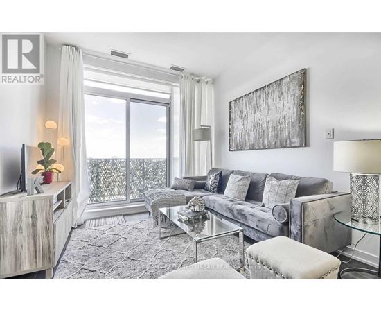 A living room with a grey couch, a glass table, and a large window with a view of the balcony.