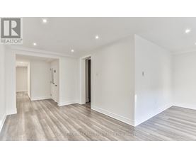 A spacious room with wood flooring and white walls.