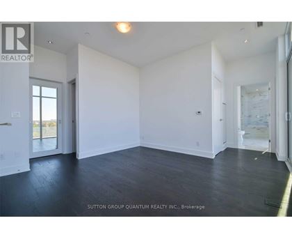 A spacious room with white walls and dark wood flooring.