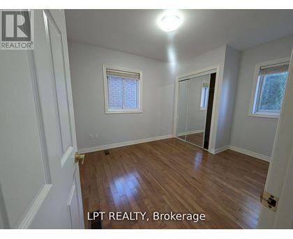 A room with wooden flooring and white walls, with a window and a door visible.