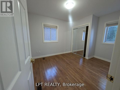 A room with wooden flooring and white walls, with a window and a door visible.