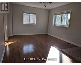 A room with wooden flooring and two windows.