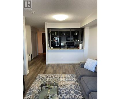 A living room with a grey couch and a coffee table in front of a kitchen area.