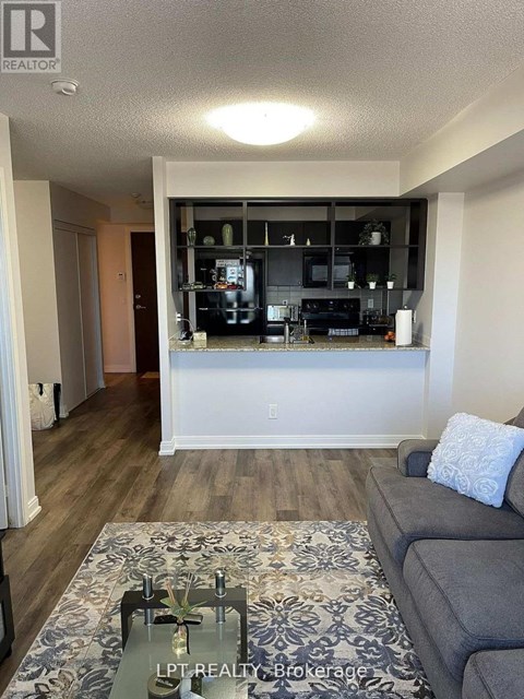 A living room with a grey couch and a coffee table in front of a kitchen area.