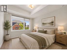 A bedroom with a large bed, a nightstand, and a window overlooking a residential area.