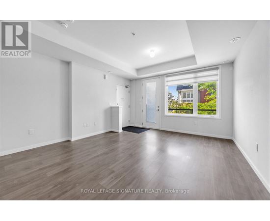 A spacious room with wooden flooring and white walls, with a window showing an outdoor view.