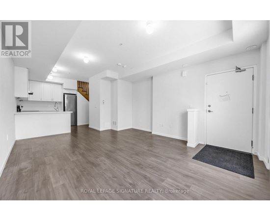 A spacious room with wooden flooring and white walls, featuring a kitchen area with white cabinets and a countertop.