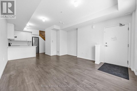 A spacious room with wooden flooring and white walls, featuring a kitchen area with white cabinets and a countertop.