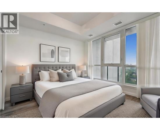 A bedroom with a large bed, a nightstand with a lamp, and a window with a view.