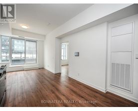 A spacious room with wooden floors and white walls, with a large window and a door on the right side.