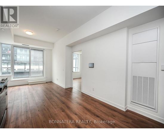 A spacious room with wooden floors and white walls, with a large window and a door on the right side.