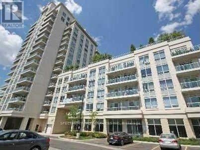A tall residential building with multiple balconies and cars parked in front.
