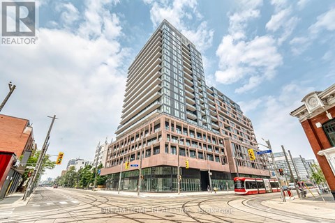 A tall building with many windows is in the center of a street corner.
