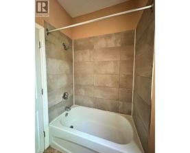 A white bathtub in a bathroom with beige tiles.