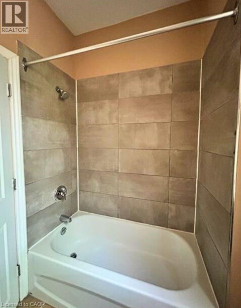 A white bathtub in a bathroom with beige tiles.