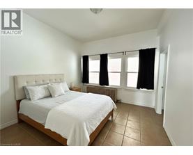 A bedroom with a bed, two pillows, a radiator, and a window with black curtains.