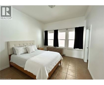 A bedroom with a bed, two pillows, a radiator, and a window with black curtains.