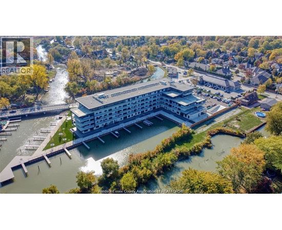 A large building with a waterfront is surrounded by trees.