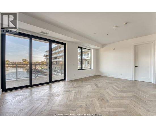 A spacious room with wooden flooring and large windows overlooking a pool area.