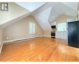 A spacious room with wooden flooring and a black refrigerator.
