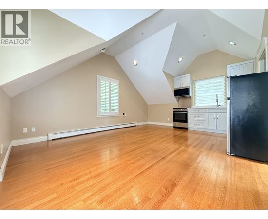 A spacious room with wooden flooring and a black refrigerator.