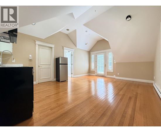 A spacious room with wooden flooring and a black piano on the left side.